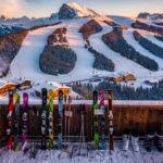 Aerial view of snow-covered Alpine ski slopes at golden hour with colorful affordable ski equipment on wooden lodge deck
