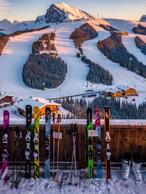 Aerial view of snow-covered Alpine ski slopes at golden hour with colorful affordable ski equipment on wooden lodge deck