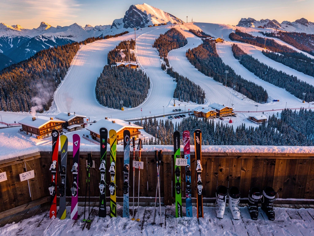 Aerial view of snow-covered Alpine ski slopes at golden hour with colorful affordable ski equipment on wooden lodge deck