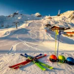 Luchtfoto van besneeuwde skipistes in Mittelberg met ski-uitrusting, chalets en skiliften onder blauwe hemel