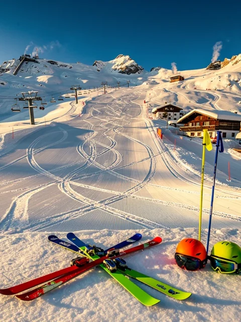 Luchtfoto van besneeuwde skipistes in Mittelberg met ski-uitrusting, chalets en skiliften onder blauwe hemel