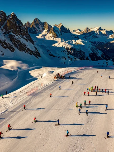 Luchtfoto van besneeuwde skipistes in Neustift im Stubaital met kleurrijke skigroepen op verschillende hellingen