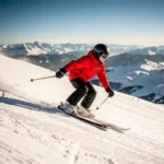 Beginner skiër in rood jack maakt een ploegbocht op steile gepiste Alpenhelling, met wit bergpanorama onder stralende middagzon.