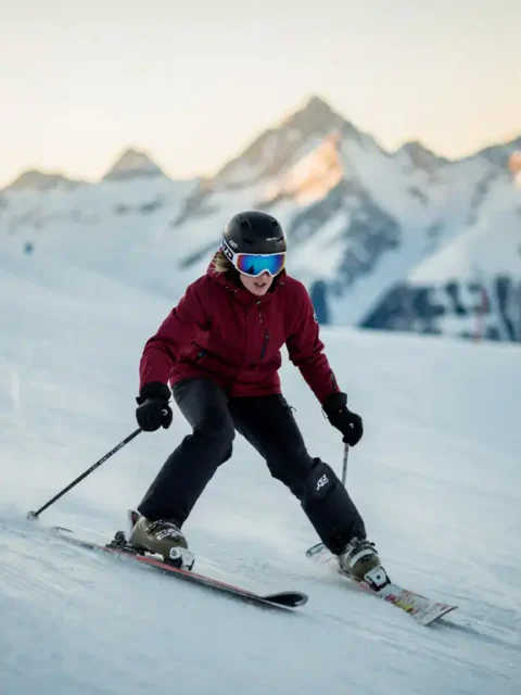 Beginner skiër in sneeuwploegpositie op zachte helling, knieën naar binnen gebogen, skitoppen in V-vorm, Alpiene toppen op de achtergrond.