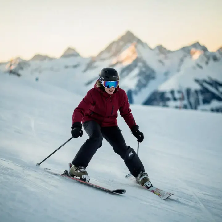 Beginner skiër in sneeuwploegpositie op zachte helling, knieën naar binnen gebogen, skitoppen in V-vorm, Alpiene toppen op de achtergrond.