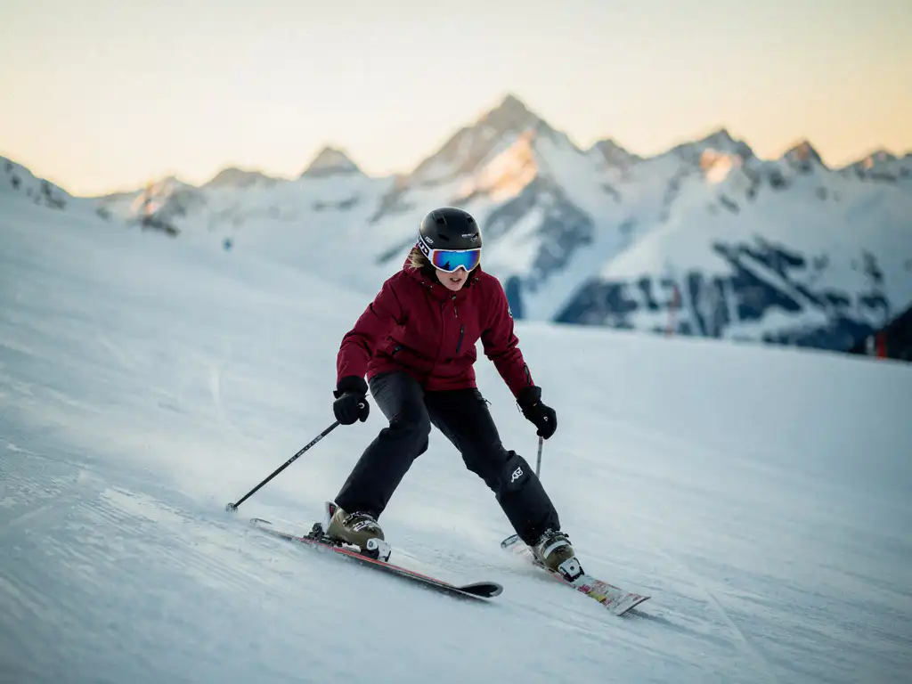 Beginner skiër in sneeuwploegpositie op zachte helling, knieën naar binnen gebogen, skitoppen in V-vorm, Alpiene toppen op de achtergrond.