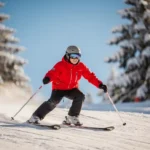Beginner skiër in felrood jack maakt een ploegbocht op een zacht glooiende, verzorgde piste met besneeuwde dennenbomen op de achtergrond.