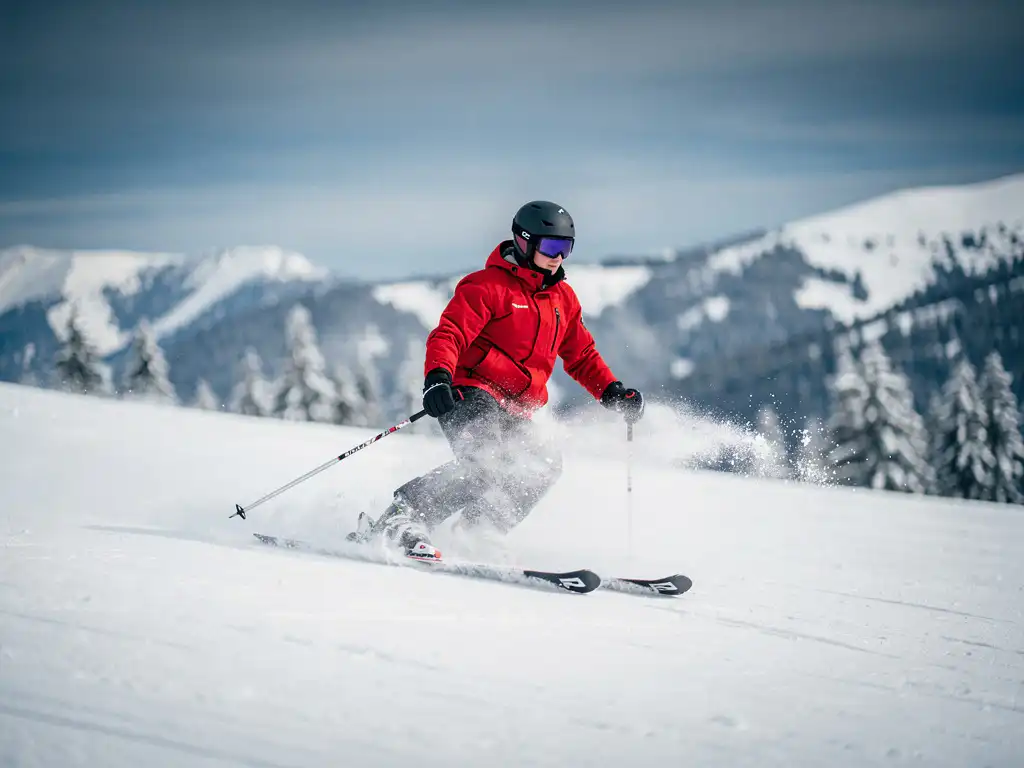 Beginner skiër op verzorgde alpine piste in rood jack, maakt onzekere bocht met skis naar buiten, verse sneeuw spat omhoog.
