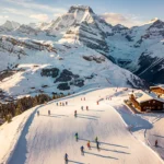 Aerial view of Combloux ski slopes with Mont Blanc mountain backdrop, skiers on groomed runs, and traditional alpine chalets