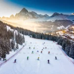 Aerial view of Courchevel 1300 ski slopes with skiers practicing on groomed runs surrounded by snow-covered Alpine peaks