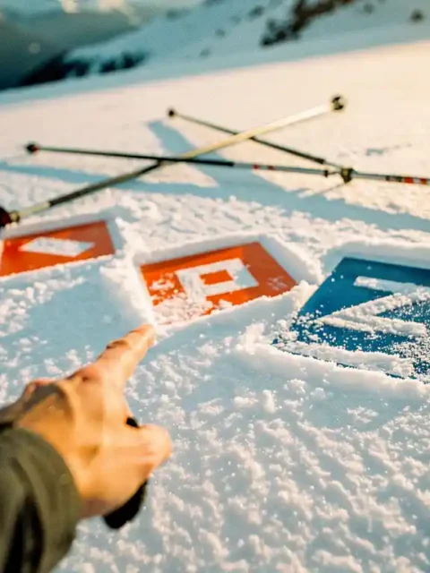 Main gantée d'instructeur de ski pointant vers des balises de piste colorées dans la poudreuse fraîche en montagne