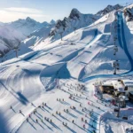 Aerial view of Isola 2000 ski resort with groomed slopes, ski lesson groups, and snow-covered Alpine peaks in morning sunlight.