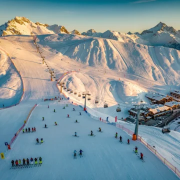 Luchtfoto van Isola 2000 skigebied met besneeuwde Alpentoppen, skipistes en skiërs op verschillende moeilijkheidsgraden