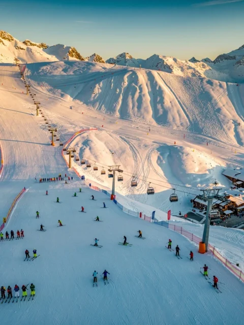 Luchtfoto van Isola 2000 skigebied met besneeuwde Alpentoppen, skipistes en skiërs op verschillende moeilijkheidsgraden