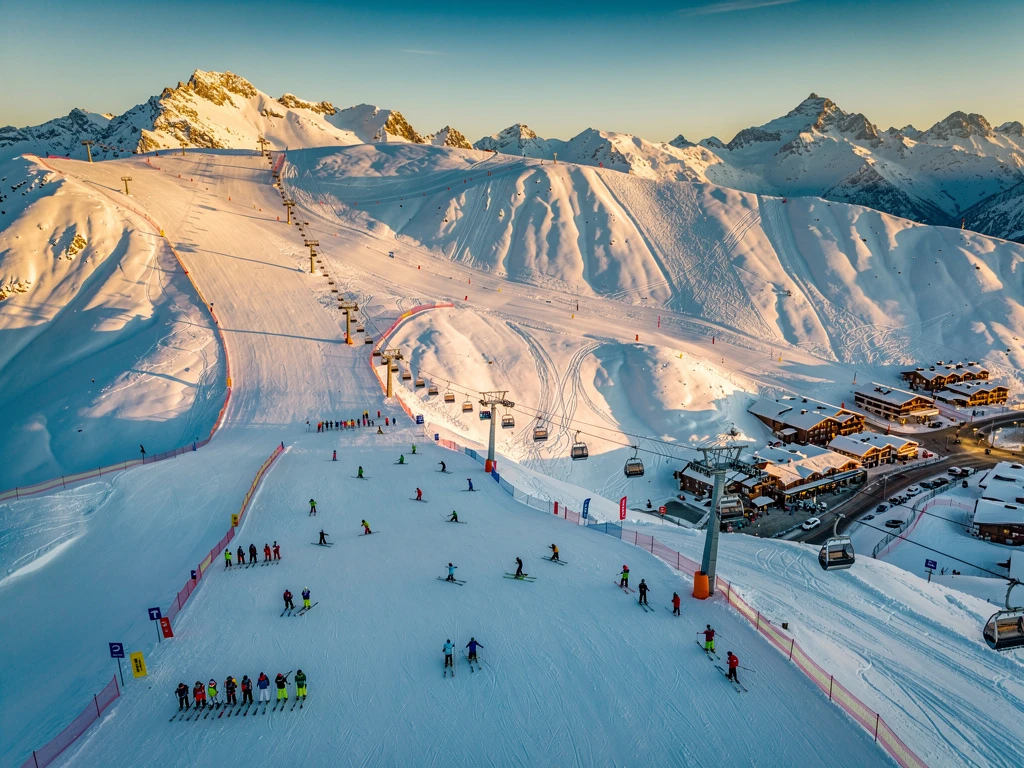 Luchtfoto van Isola 2000 skigebied met besneeuwde Alpentoppen, skipistes en skiërs op verschillende moeilijkheidsgraden