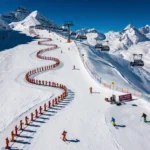 Aerial view of Kaltenbach ski slopes with instructors leading colorful groups down groomed Alpine runs under blue skies.