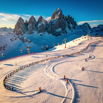 Aerial view of Kaprun ski slopes with colorful ski groups creating curved tracks in fresh snow, Austrian peaks in background