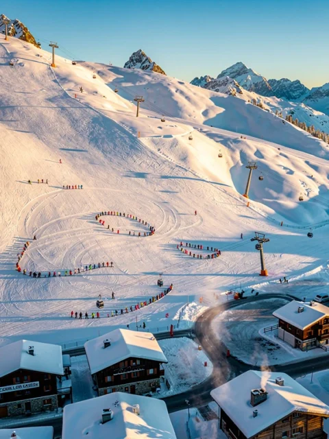Luchtfoto van Les Carroz d'Arâches skigebied met besneeuwde Alpenhellingen, skiërs, chalets en liften bij gouden uur