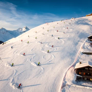 Luchtfoto van skiërs in kleurrijke winterkleding die afdalen op besneeuwde hellingen van Méribel met chalets onder blauwe lucht
