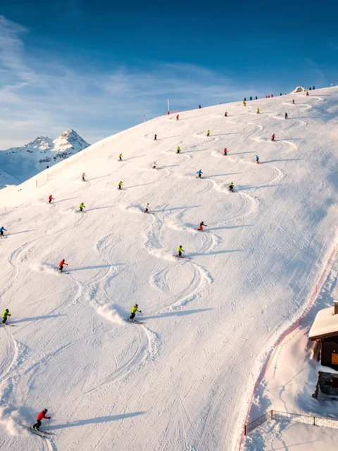Luchtfoto van skiërs in kleurrijke winterkleding die afdalen op besneeuwde hellingen van Méribel met chalets onder blauwe lucht