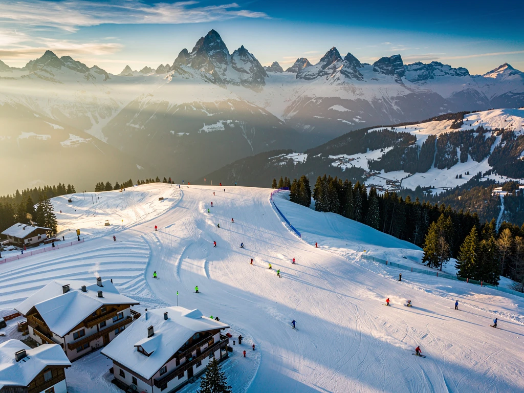 Aerial view of Mittelberg alpine ski slopes with skiers practicing on groomed runs, Austrian lodges below mountain peaks