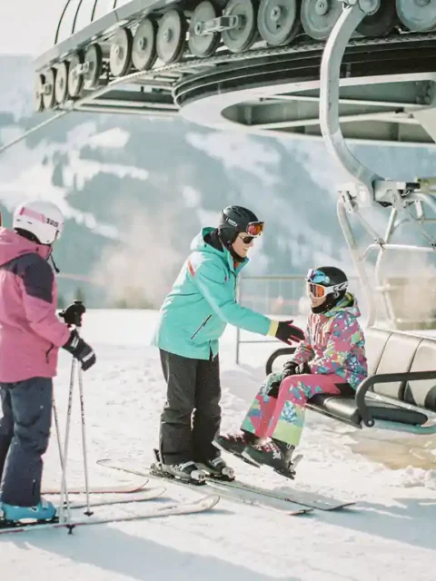 Moniteur de ski aidant un débutant nerveux à monter sur un télésiège, groupe d'étudiants sur pistes enneigées