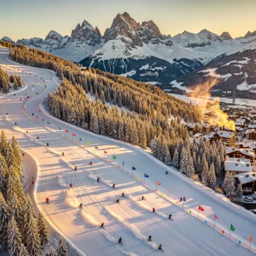 Aerial view of Morzine ski slopes at golden hour with skiers on powder snow, pine forests, and Alpine village below.