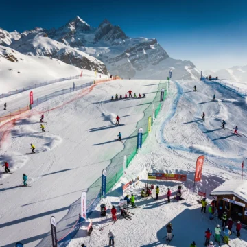 Aerial view of Orelle ski slopes with colorful skiers and instructors on groomed runs beneath snow-capped Alpine peaks.