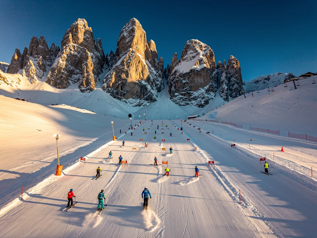 Aerial view of Scheffau am Wilden Kaiser ski slopes with instructors teaching groups on groomed runs below Alpine peaks
