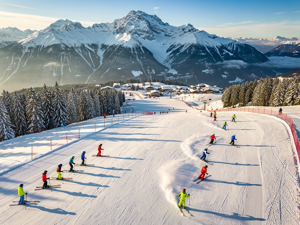 Ski instructors teaching groups on groomed alpine slopes in Schröcken, Austria during golden hour with snow-capped peaks.