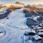 Aerial view of Schruns ski resort in Austrian Alps with ski lesson groups on groomed slopes during golden hour lighting.