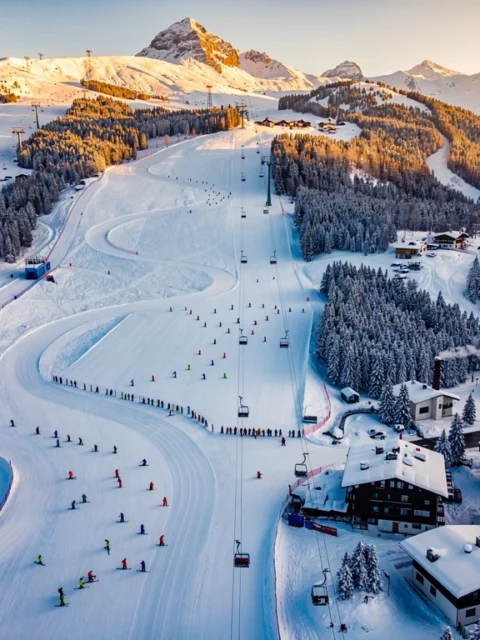 Aerial view of Schruns ski resort in Austrian Alps with ski lesson groups on groomed slopes during golden hour lighting.