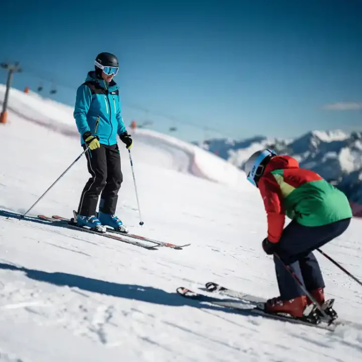Ski-instructeur met rechtopstaande houding op verzorgde alpinehelling, op de achtergrond een skiër met gebogen rug en ingezakte schouders.