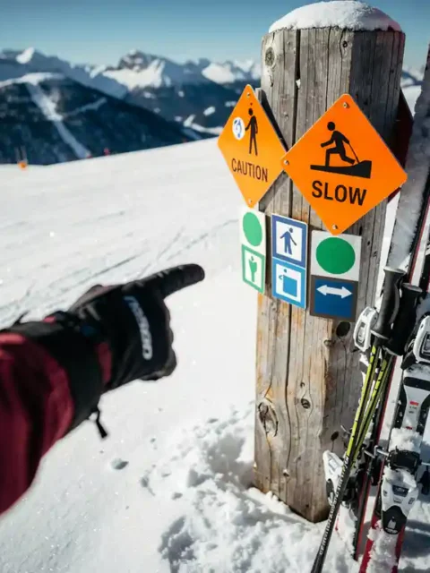 Ski-instructeur wijst naar kleurrijke piste-markeringen en waarschuwingsborden op besneeuwde berghelling