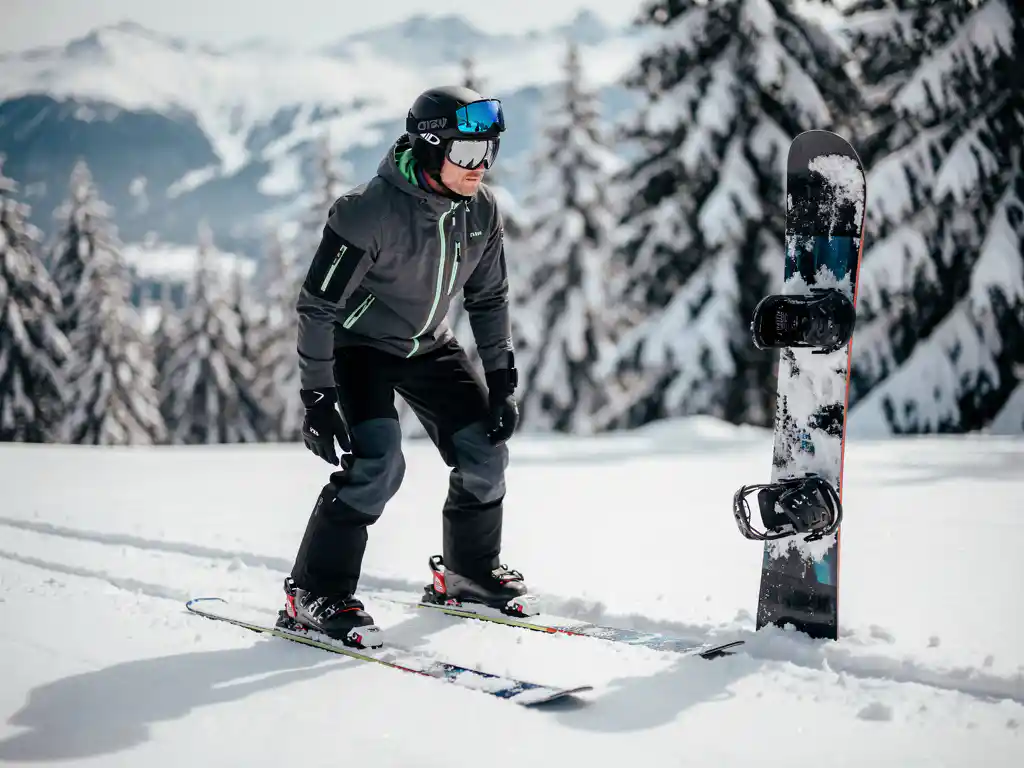 Ski-instructeur toont juiste houding naast snowboard in sneeuw, winteruitrusting zichtbaar op bergpiste