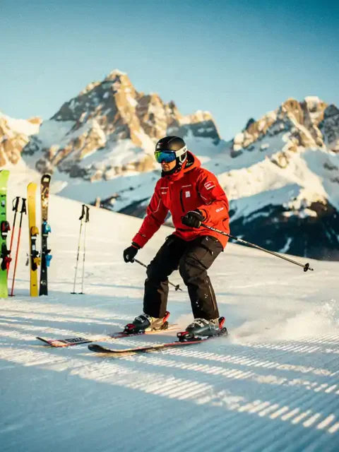 Professional ski instructor in red jacket demonstrating technique on snowy slopes with Austrian Alps in background