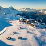 Aerial view of Les Carroz d'Arâches ski resort showing snow-covered Alpine slopes with ski groups and chalets in morning light