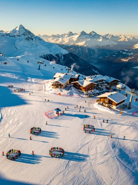 Aerial view of Les Carroz d'Arâches ski resort showing snow-covered Alpine slopes with ski groups and chalets in morning light