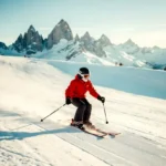 Beginnende skiër in rood jack maakt een ploegschaarwending op een brede, verzorgde blauwe piste in de Alpen.