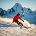 Skiër maakt een scherpe bocht op een verzorgde alpiene piste, knieën diep gebogen, poedersneeuw spat van de ski's onder stralende middagzon.