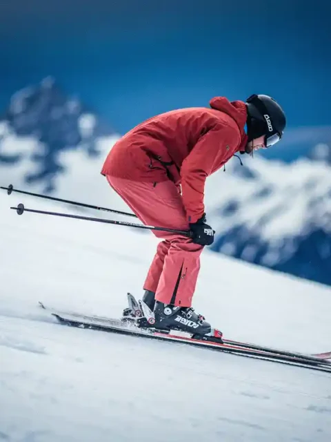 Skiër met verkeerde houding op verzorgde alpinepiste, onderrug gebogen en knieën verkeerd uitgelijnd, witte sneeuw en blauwe berglucht op achtergrond.