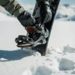 Snowboarder inspecteert bindingen en gespen van snowboard in verse sneeuw, handen met handschoenen controleren uitrusting