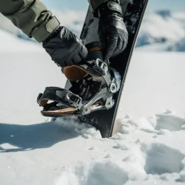 Snowboarder inspecteert bindingen en gespen van snowboard in verse sneeuw, handen met handschoenen controleren uitrusting