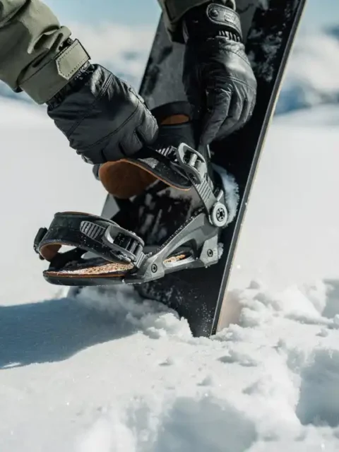 Snowboarder inspecteert bindingen en gespen van snowboard in verse sneeuw, handen met handschoenen controleren uitrusting