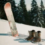 Gebruikte snowboard met slijtageplekken tegen verse poedersneeuw op bergpiste, versleten snowboardlaarzen ernaast