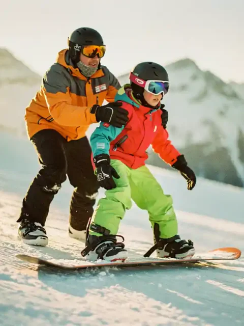 Snowboard instructeur helpt beginner met juiste houding op besneeuwde helling, bergen op achtergrond