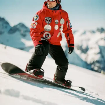 Professionele snowboard instructeur met certificatie badges op rode jas demonstreert techniek op poedersneeuw