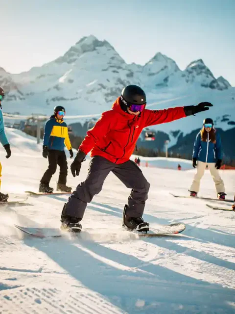 Snowboard instructeur toont techniek aan studenten op besneeuwde berghelling met bergtoppen op achtergrond