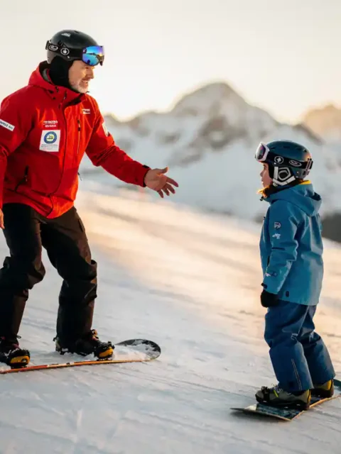 Professionele snowboard instructeur in rode jas toont juiste houding aan beginnende student op besneeuwde piste