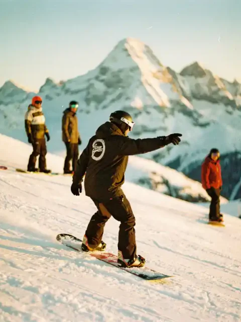 Snowboard instructeur toont techniek aan studenten op besneeuwde bergpiste met zonneschijn en bergtoppen op achtergrond